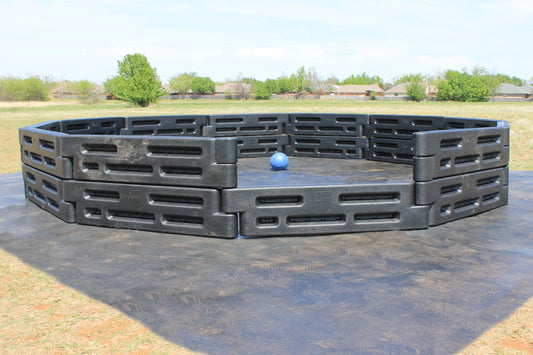 Outdoor gaga ball pit made of modular black plastic panels with a blue ball on a rubber play surface by Castle Sports.